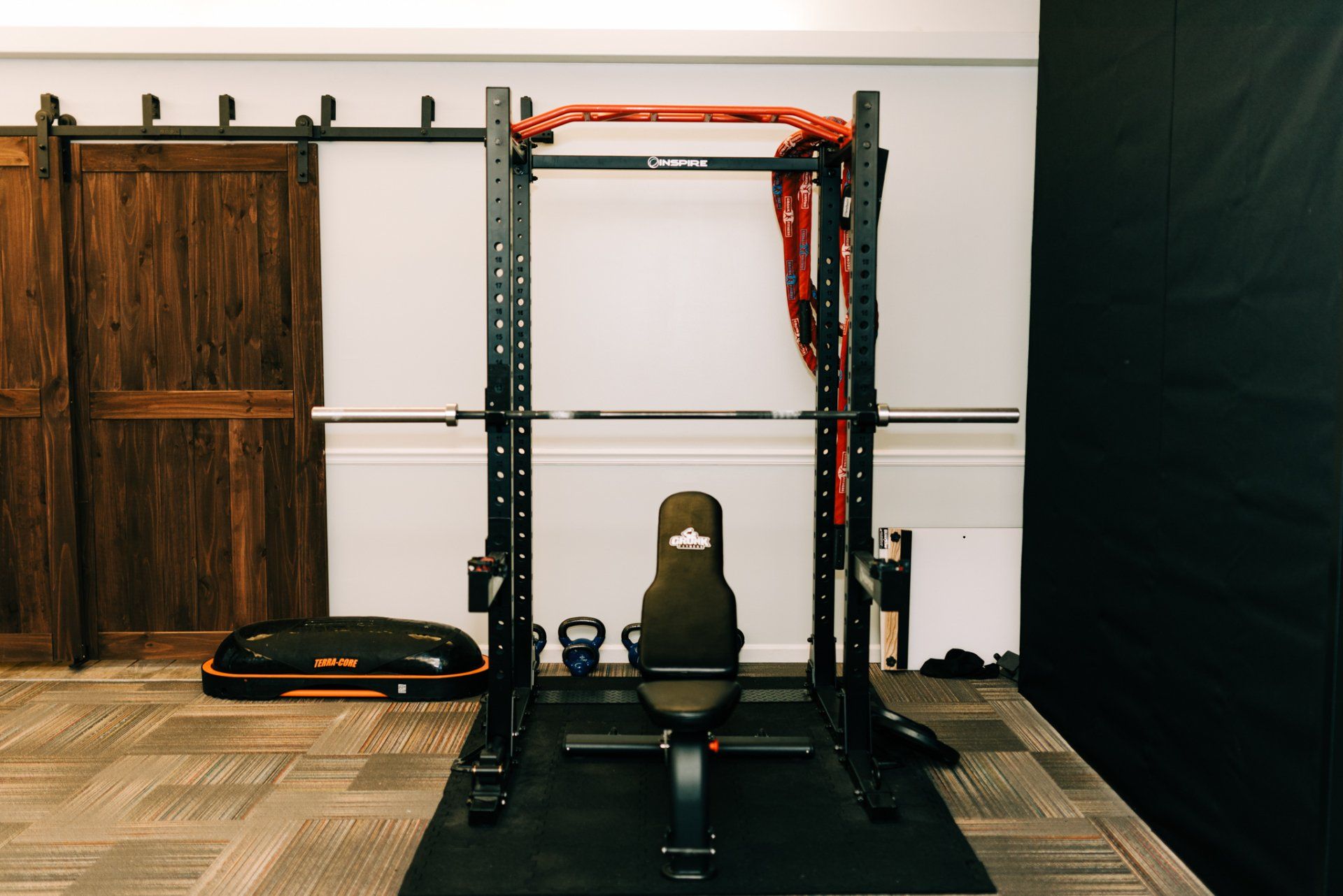 A gym with a bench , barbells , and a sliding barn door.