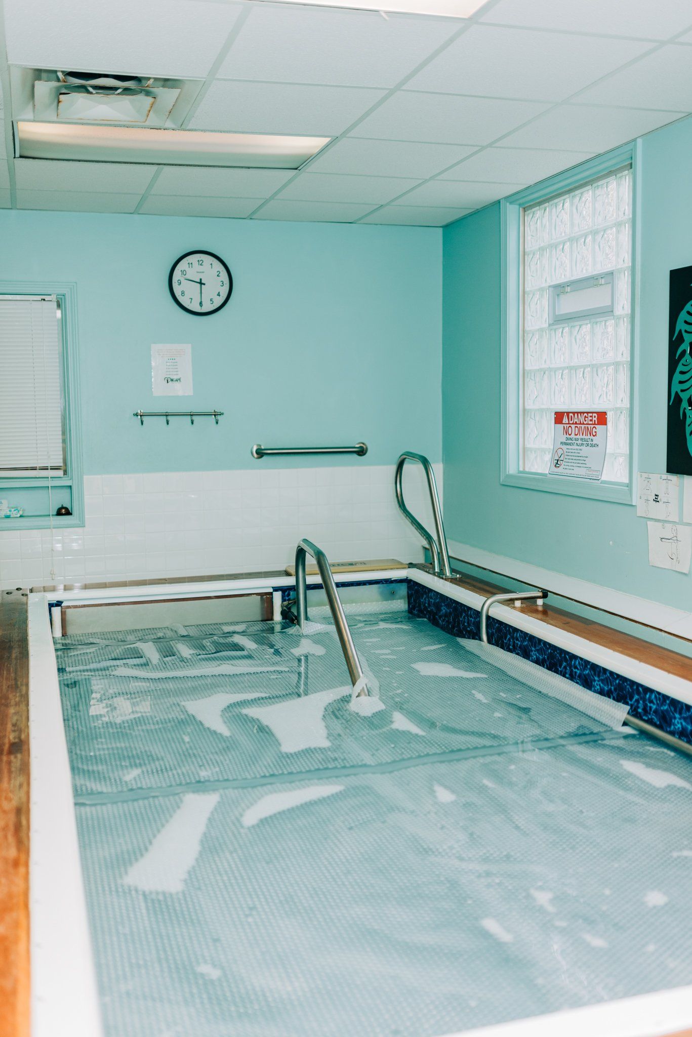 A large swimming pool in a room with a clock on the wall.