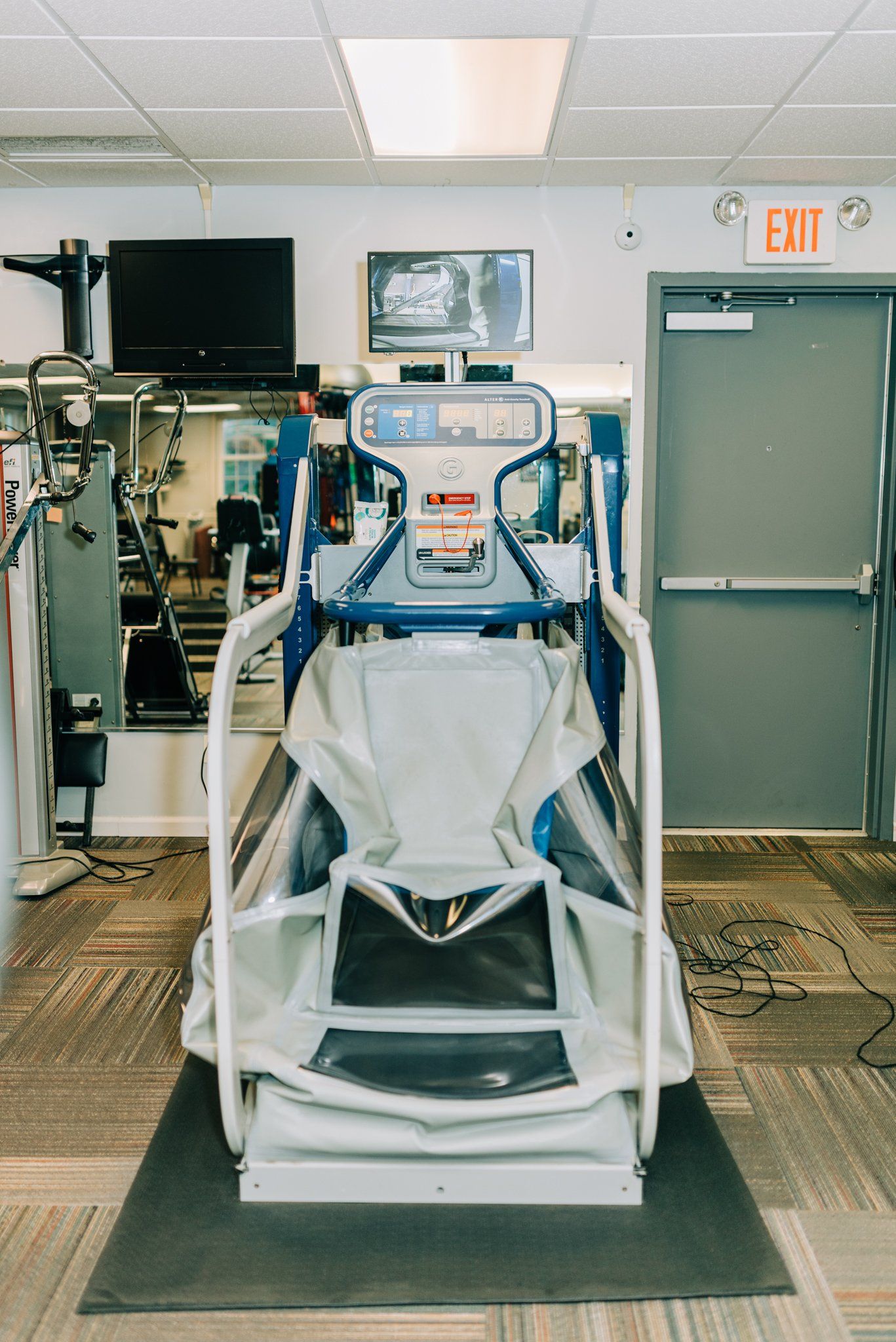 A treadmill is sitting in a gym next to an exit sign.
