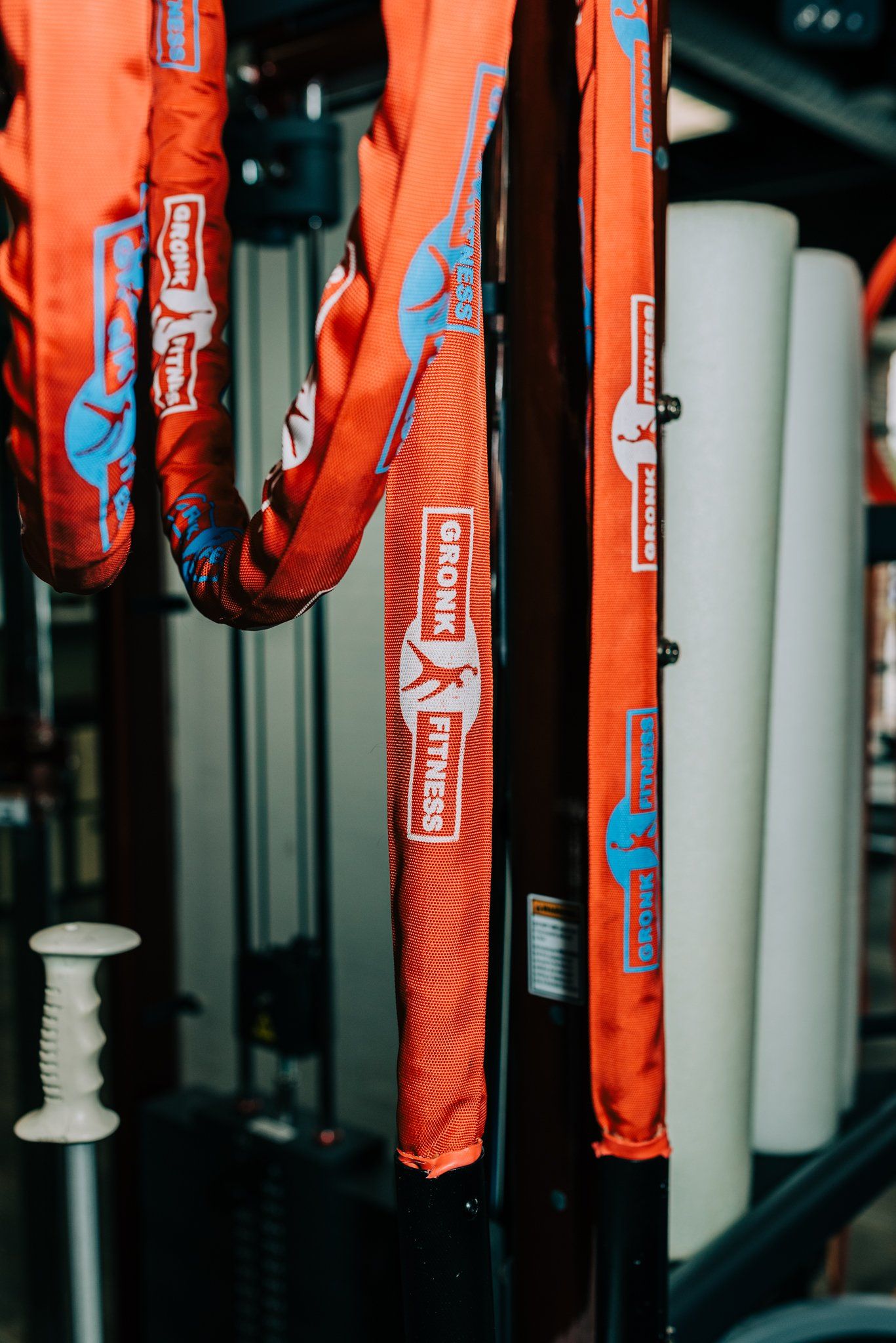A bunch of orange ropes are hanging from a rack in a gym.