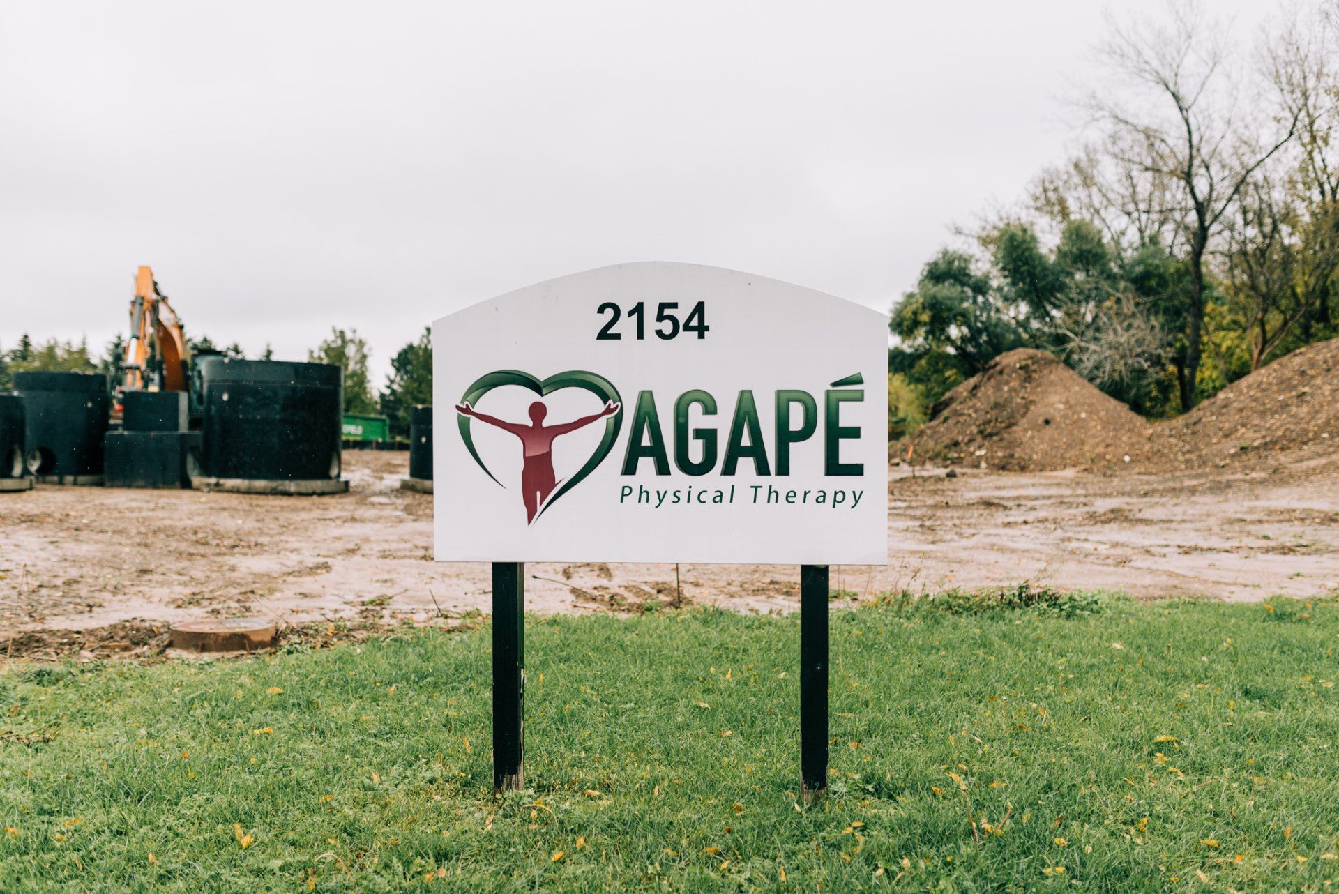 A sign for agape physical therapy is sitting in a grassy field.