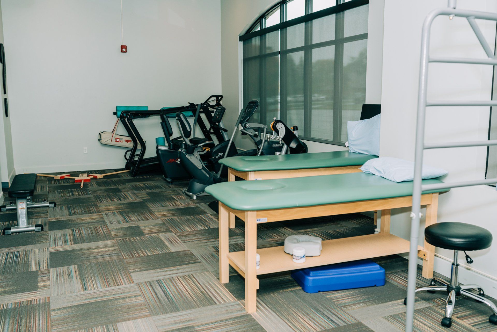 A physical therapy room with two green tables and a ladder.