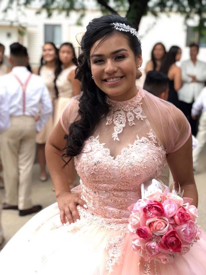 Woman in a blush lace gown holding pink bouquet outdoors, smiling at a formal event.