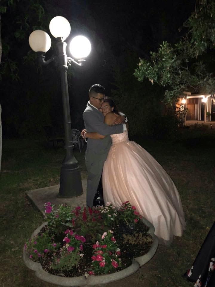 Couple embracing beside a lit lamp post and flower bed at night in a garden setting