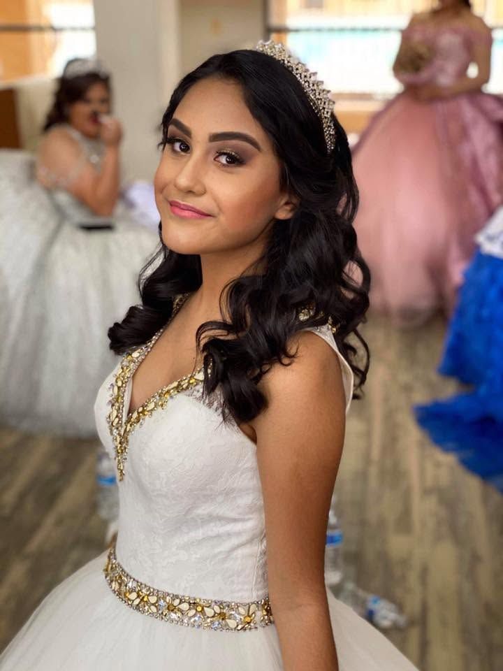 Woman in a white and gold gown smiling at a formal event with blurred guests in the background