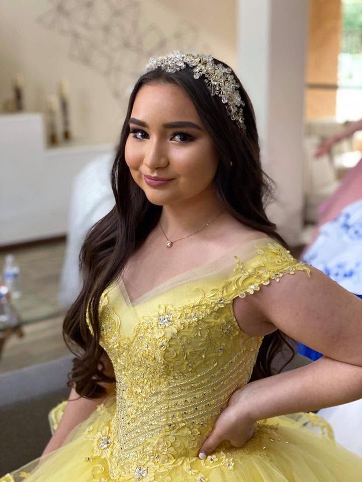 Young woman in a yellow gown and jeweled headband posing indoors with one hand on her hip