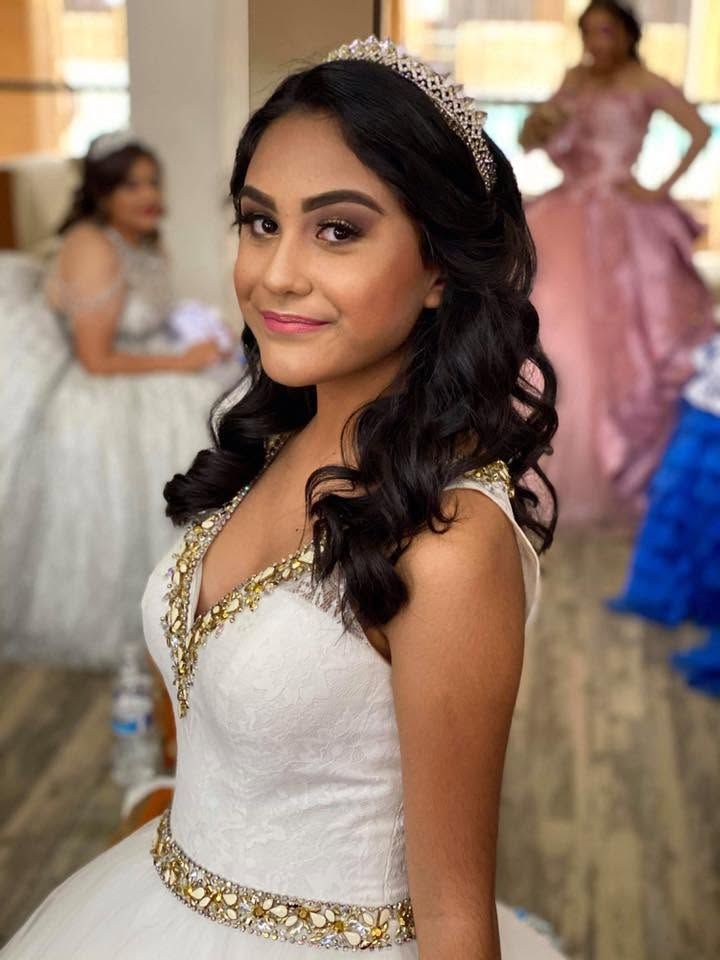 Woman in a white and gold gown smiling at a formal event with guests in the background