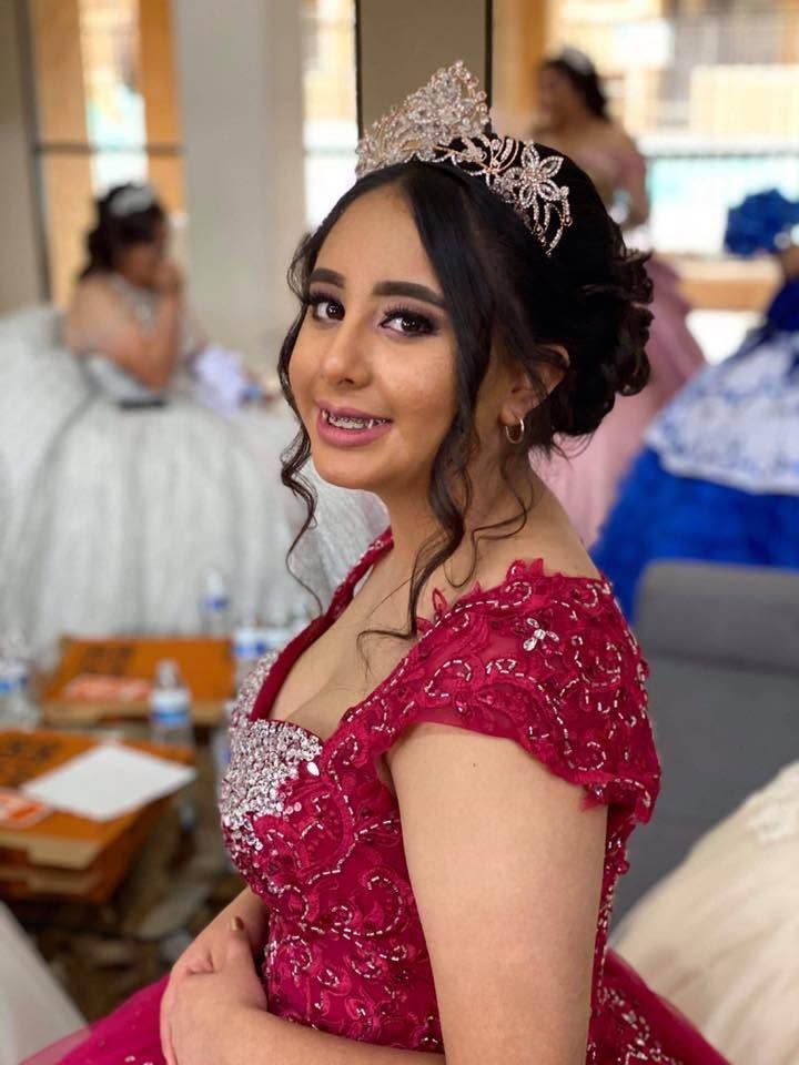 Woman in a red sequined dress and tiara smiling at an indoor celebration table