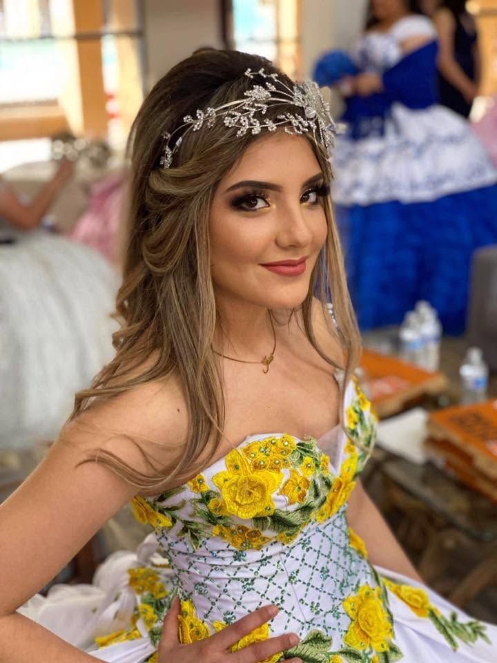 Woman in a yellow floral dress and jeweled headband smiling at an indoor celebration.