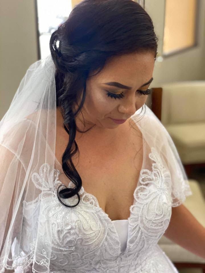 Bride in a white lace wedding dress and veil, looking down indoors.