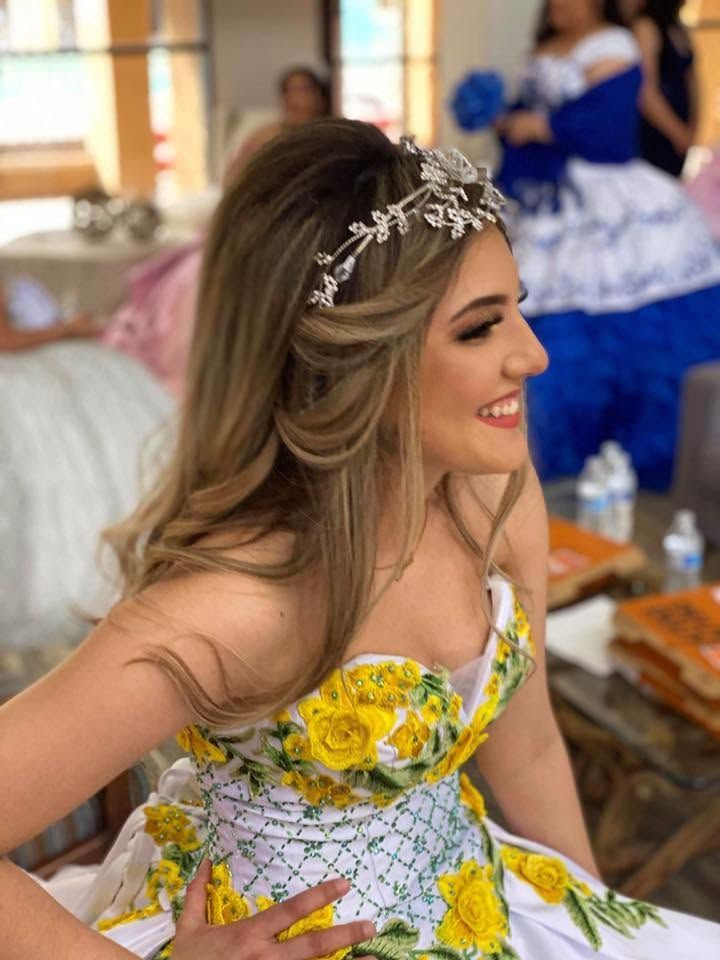 Smiling woman in a yellow-and-white floral dress wearing a jeweled headpiece at a festive indoor event