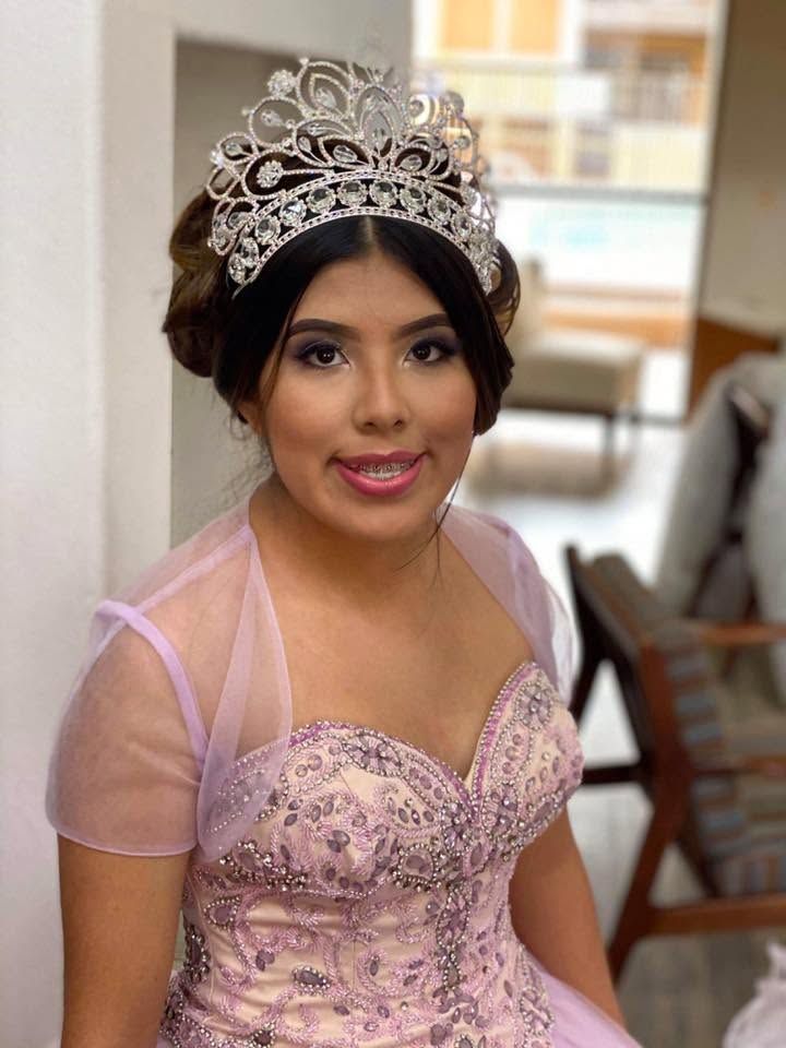 Woman in a pink embellished gown and tiara, smiling indoors at a formal event.