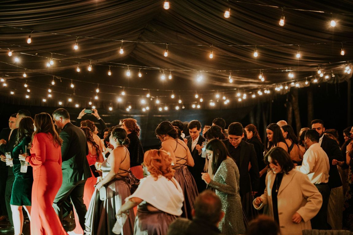 Crowded outdoor party under string lights, with people dancing and mingling at night