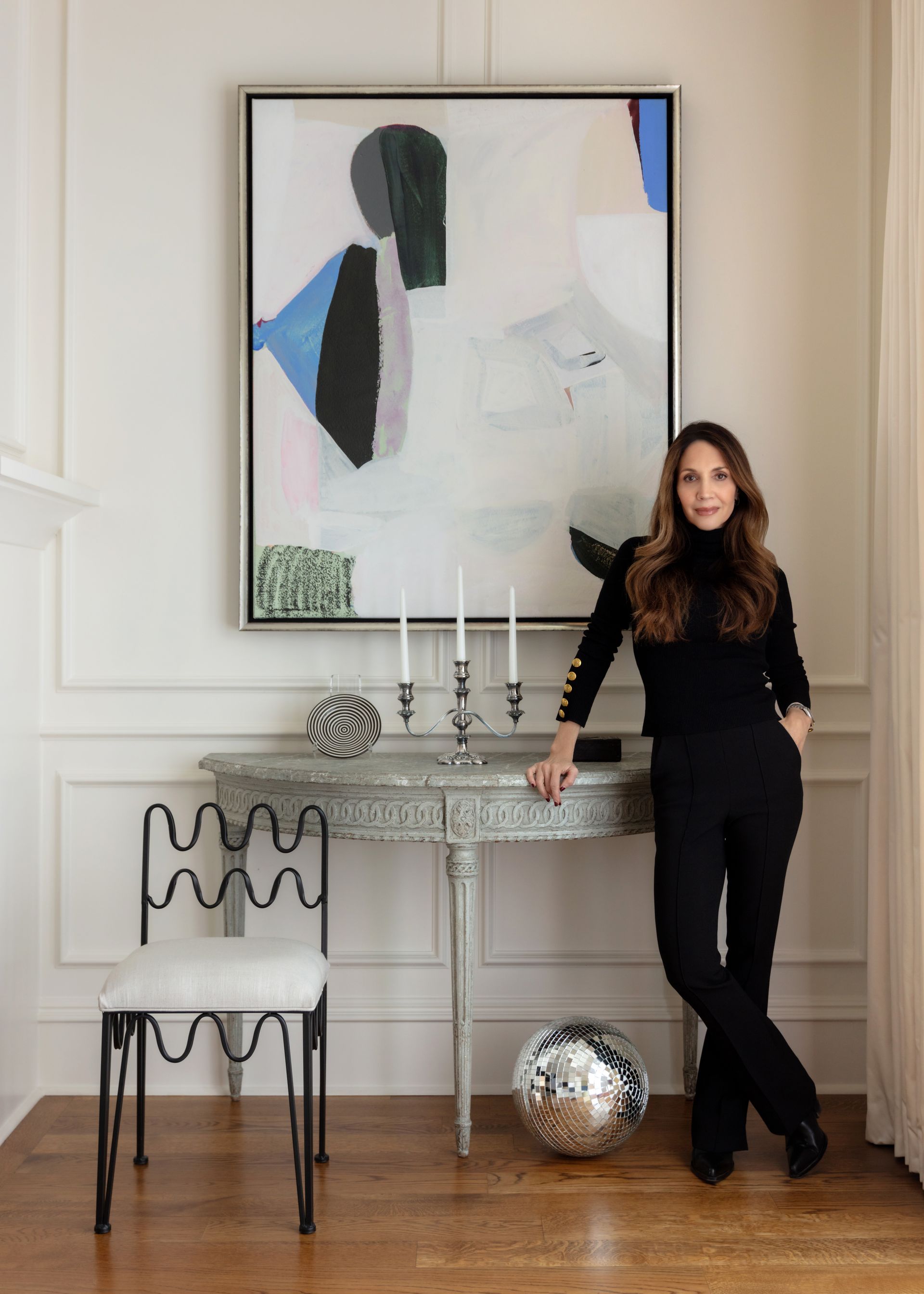 Woman in black standing by a silver console table beneath a large abstract painting.