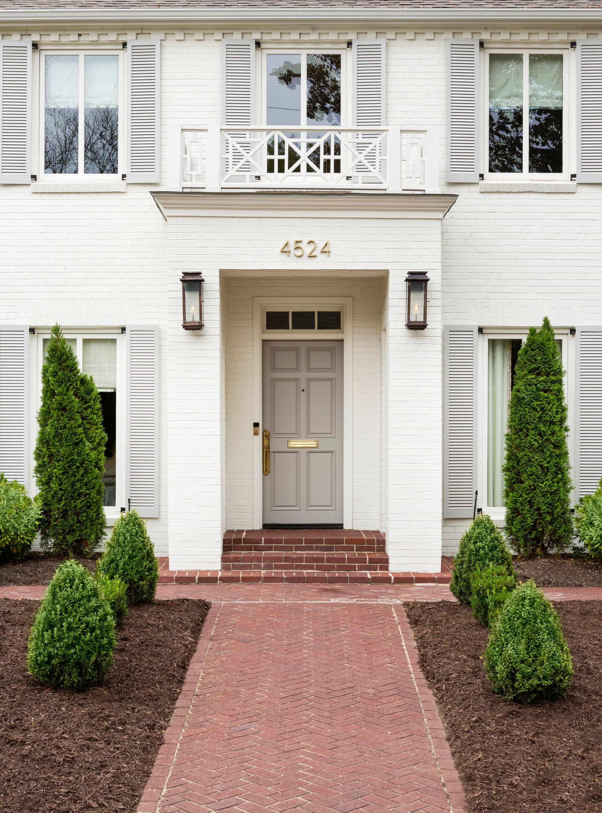 Front entrance of a white house with red walkway, black lanterns, and trimmed shrubs