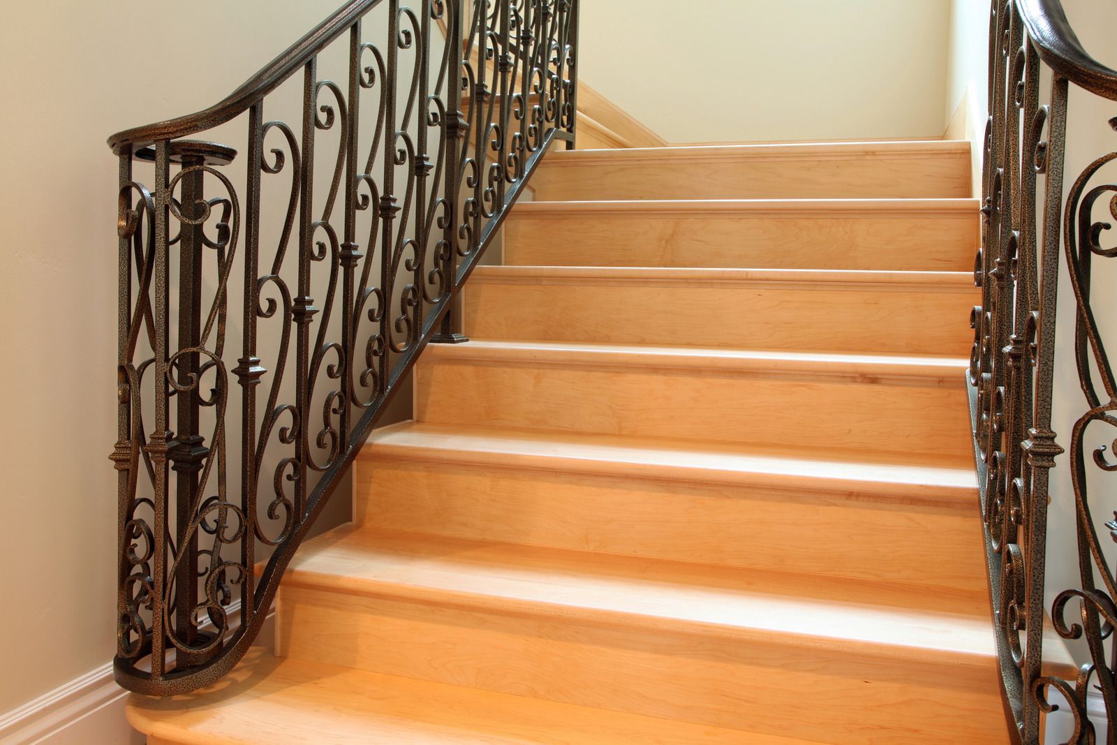 Wooden staircase with decorative wrought-iron railing against a light-colored wall.