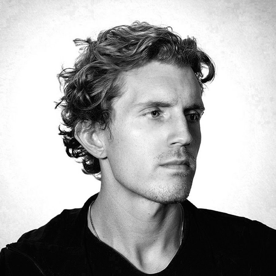 Black-and-white studio portrait of a man with curly hair, looking to the side.