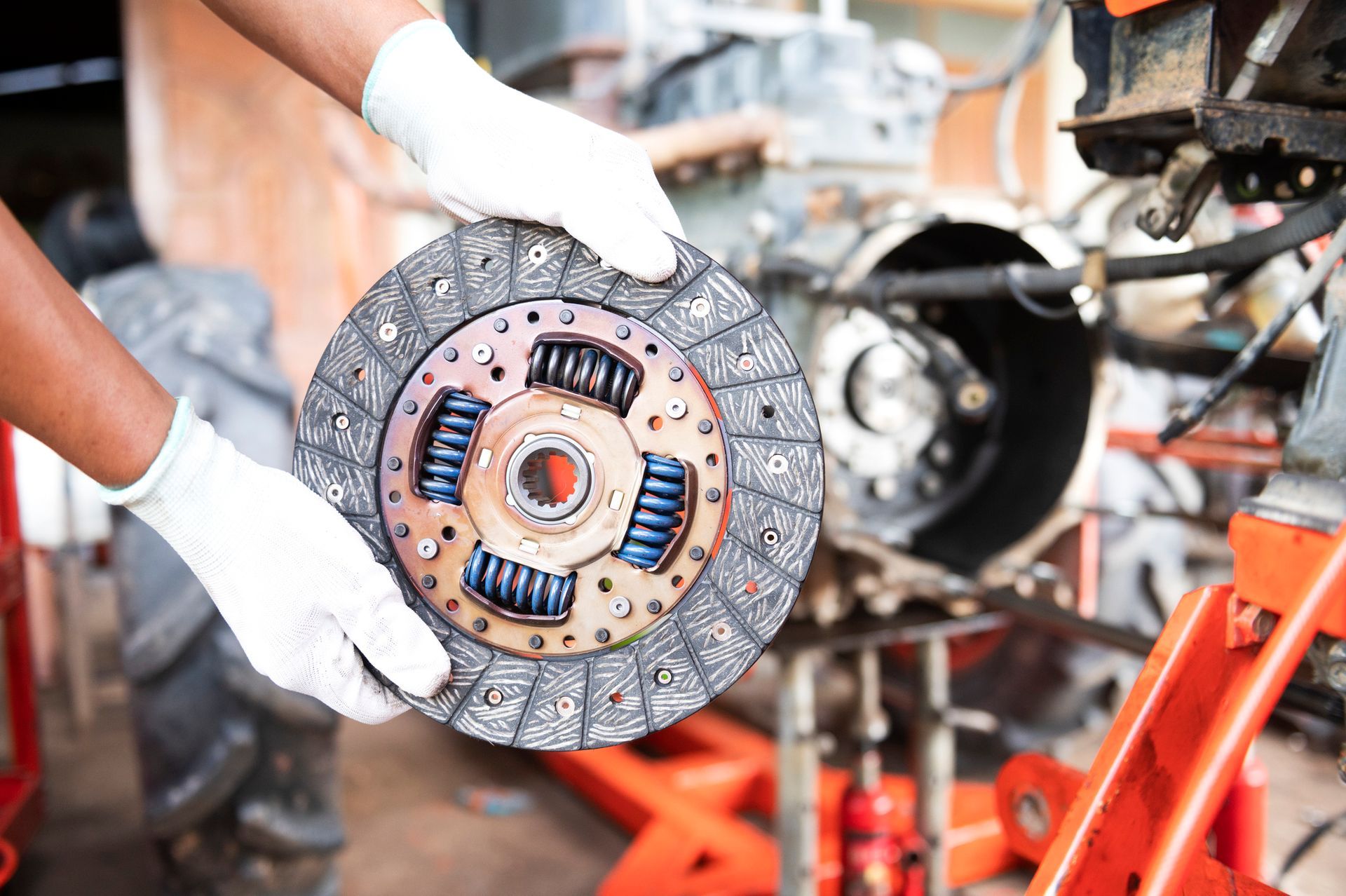 A person is holding a clutch disc in their hands in front of a car engine.