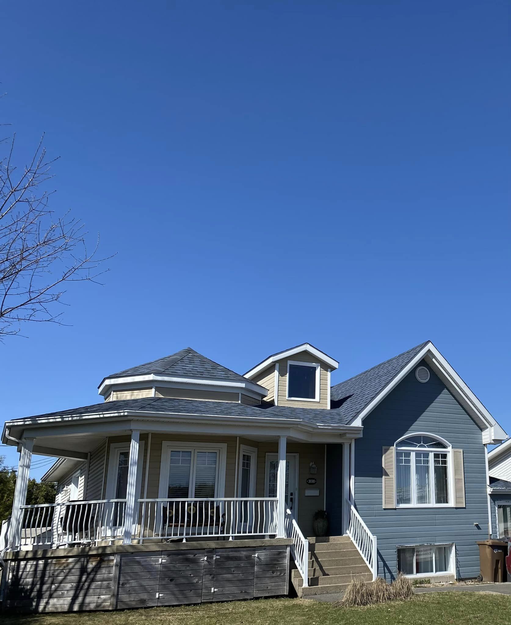 Maison bleue et beige avec porche et lucarnes sous un ciel bleu clair.