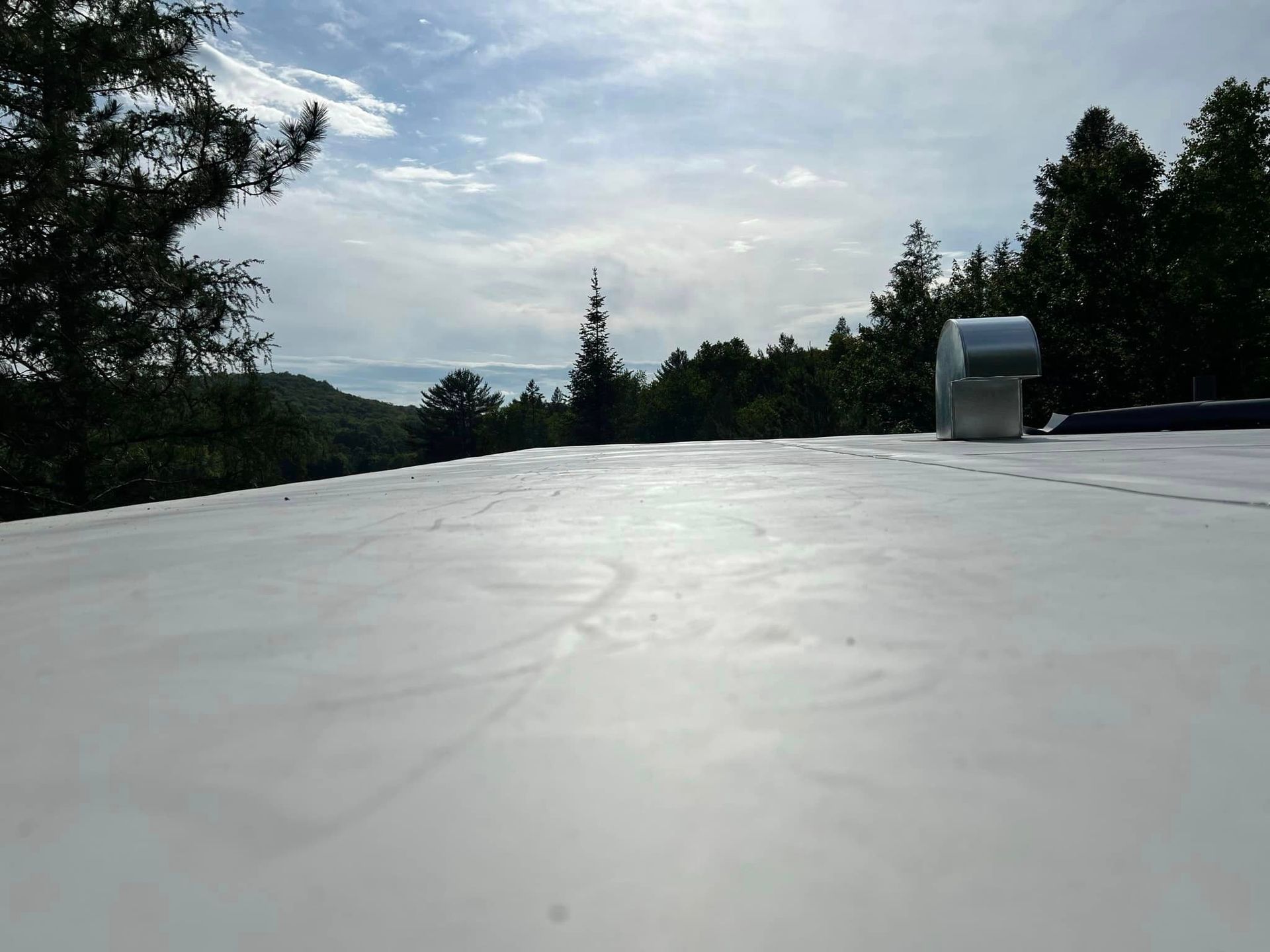 Toit blanc avec aération sur fond d'arbres, de collines au loin et de ciel.