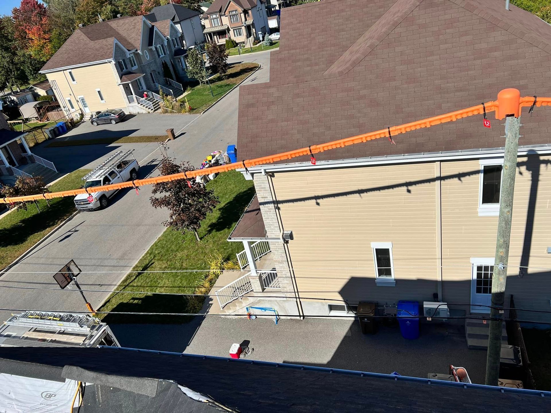 Vue aérienne d'une rue avec une maison. Un poteau électrique avec une ligne orange est visible au premier plan.