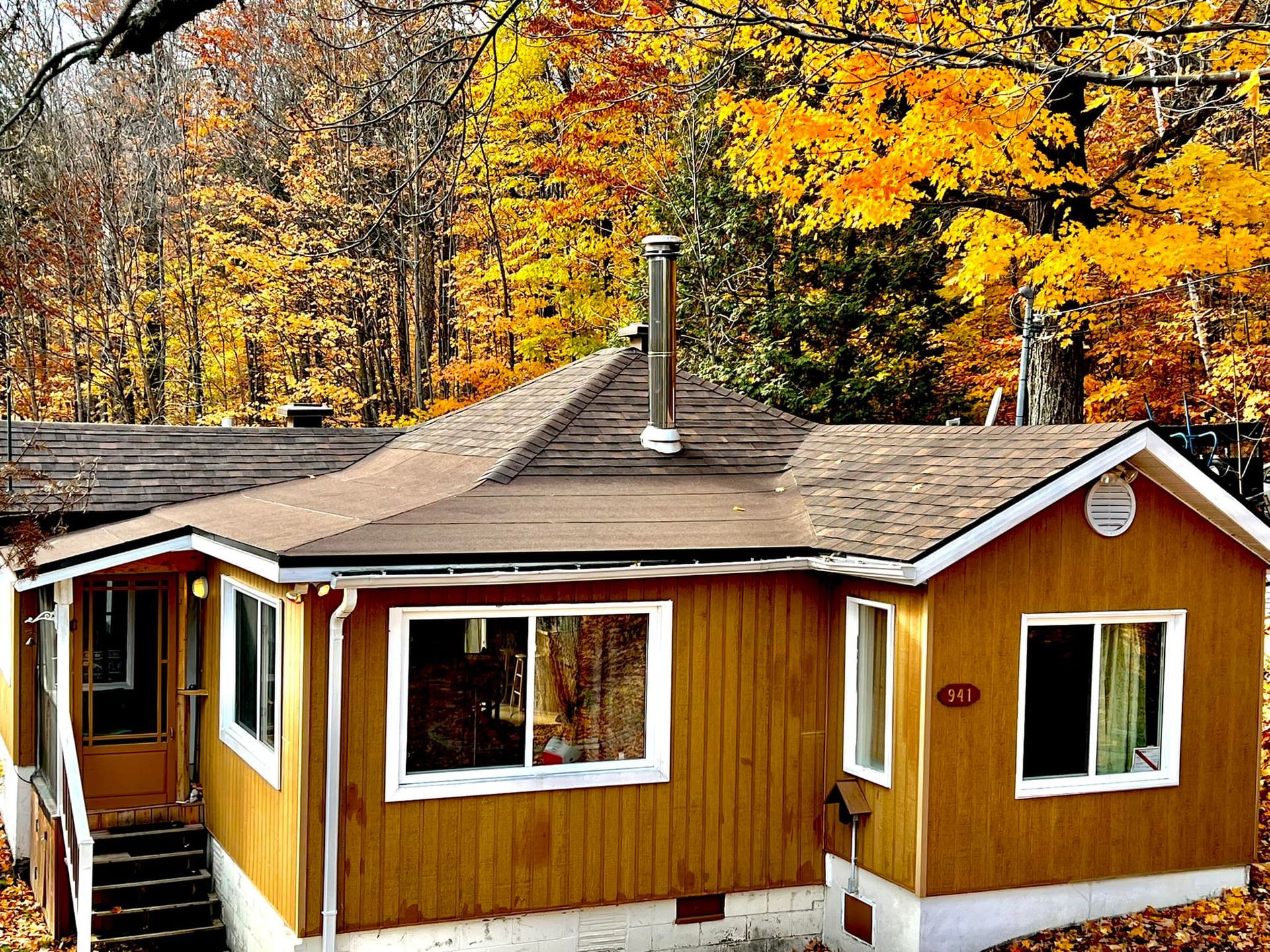 Un chalet à l'extérieur brun et à la cheminée, dans un décor de feuillage automnal.