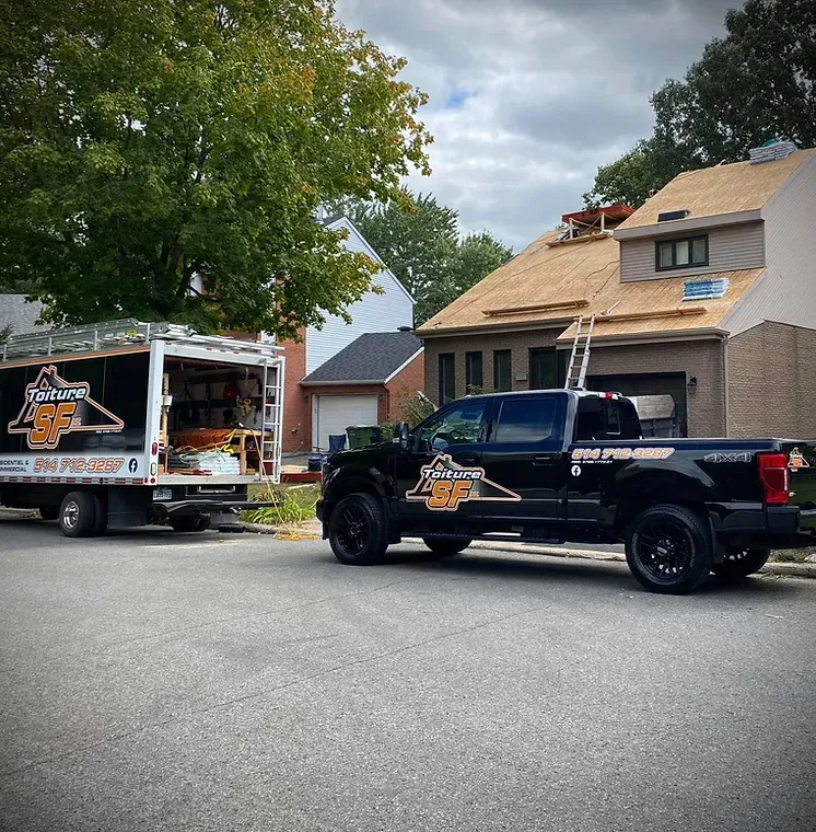 Un camion noir et un camion de chantier portant le logo « B&P Roofing » sont stationnés près d'une maison en construction.