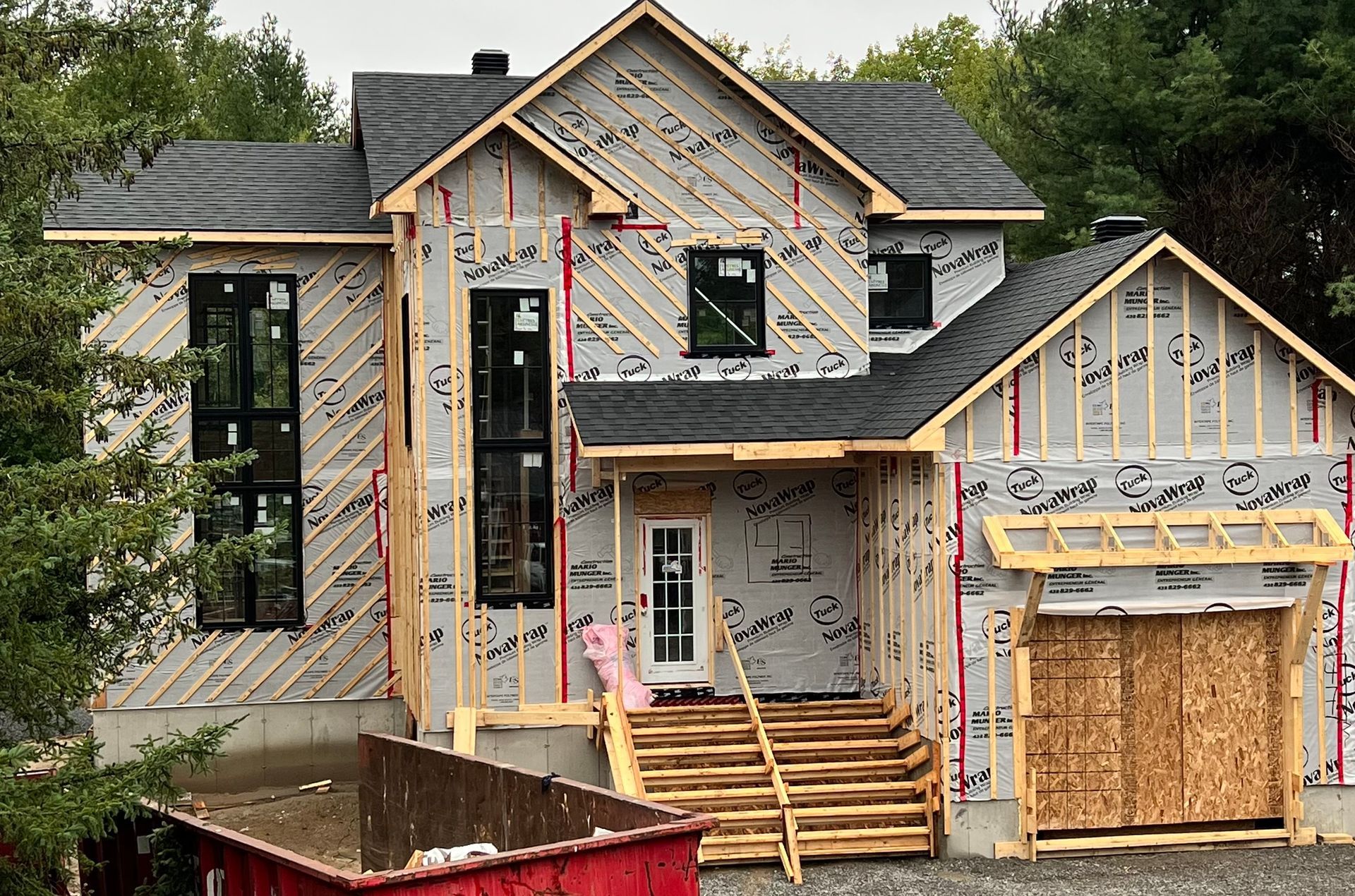Maison en construction avec charpente en bois apparente, bardage et toiture gris foncé.