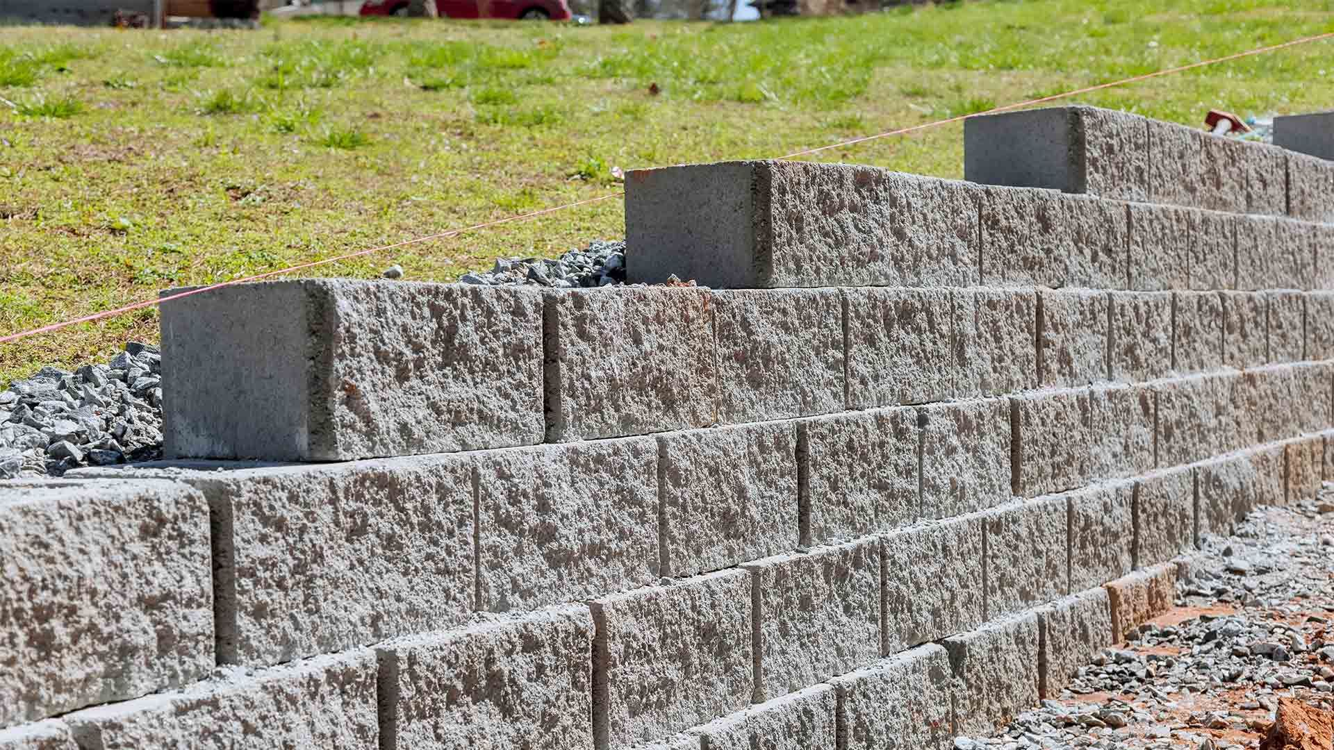 A brick wall is being built on top of a grassy hill.