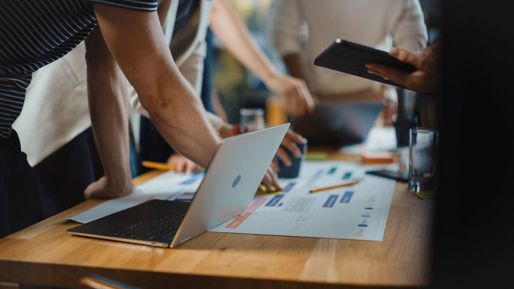 A group of people are standing around a table looking at a laptop.
