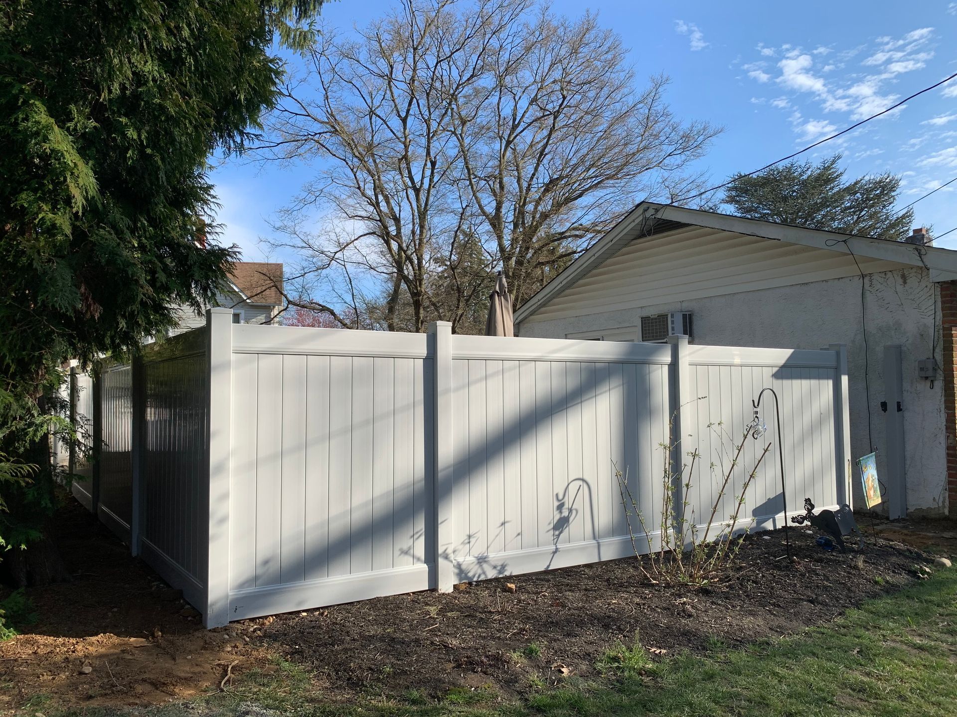 Gray vinyl fence surrounding a backyard with a building and leafless tree visible. Gray vinyl fence surrounding a backyard with a building and leafless tree visible.