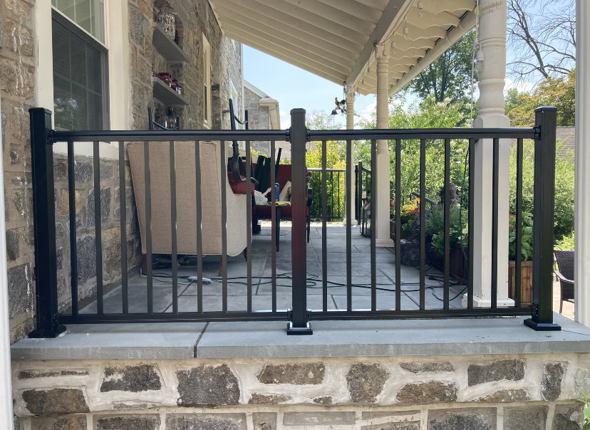 Black chain-link fence on a sloped green lawn with steps leading to a house in a residential setting.