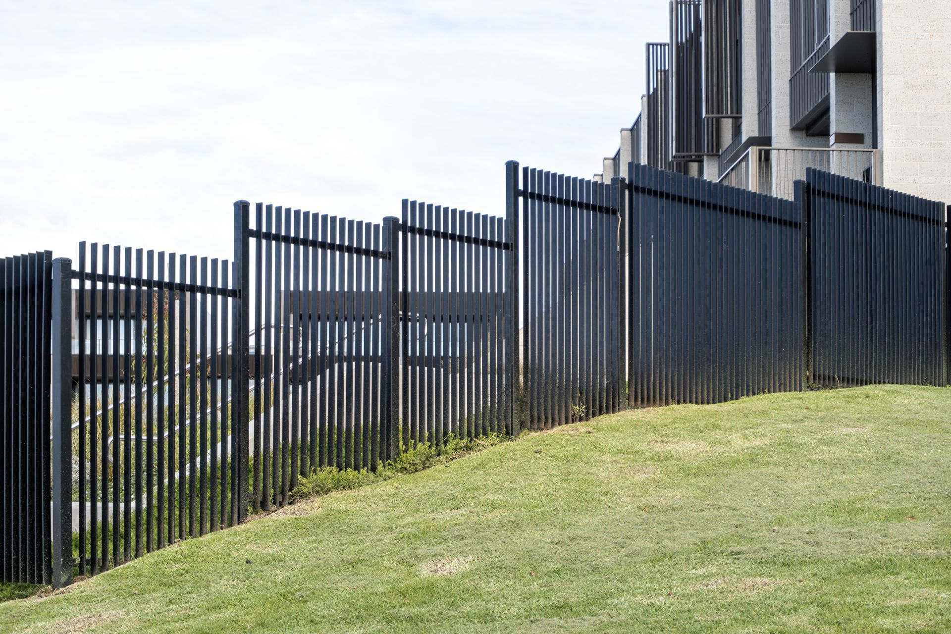 Black metal fence on a grassy hill, with a building in the background against a cloudy sky. Black metal fence on a grassy hill, with a building in the background against a cloudy sky.