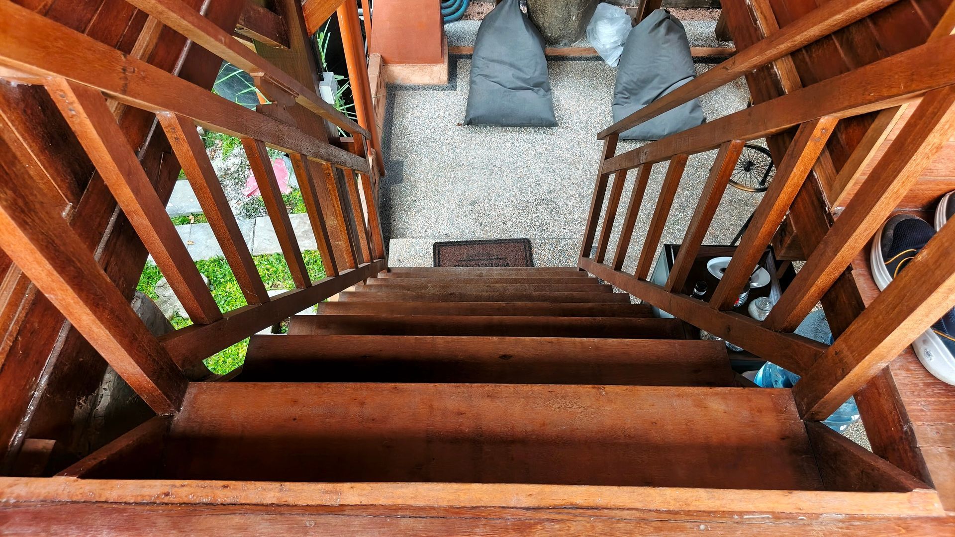 Wooden staircase leading down to a gravel area with seating and partial view of a green lawn.