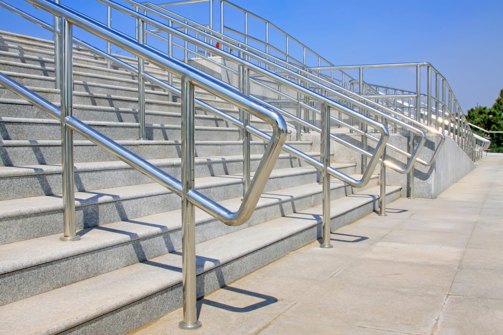Gray granite stairs with stainless steel handrails, outdoors on a sunny day.