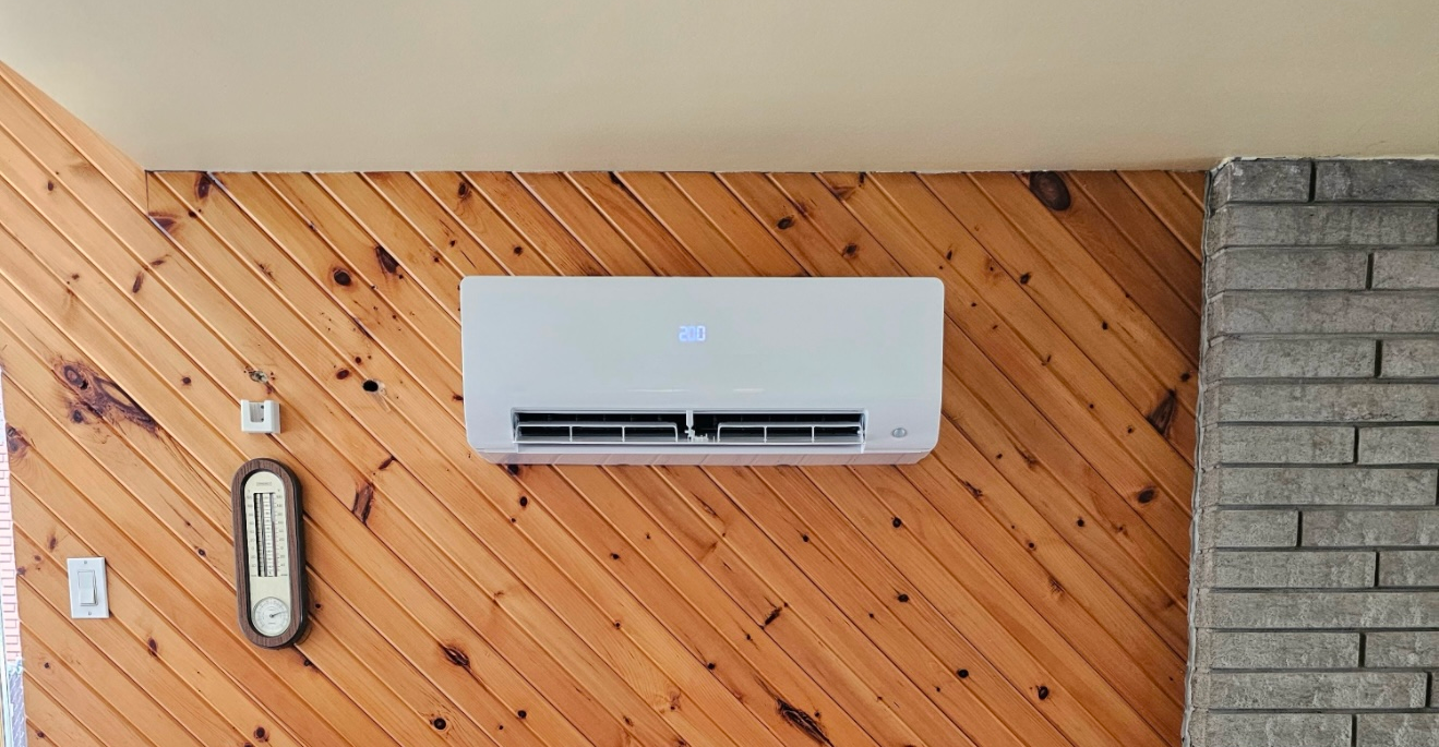 Climatiseur mural blanc sur un mur lambrissé à côté d'une cheminée en pierre