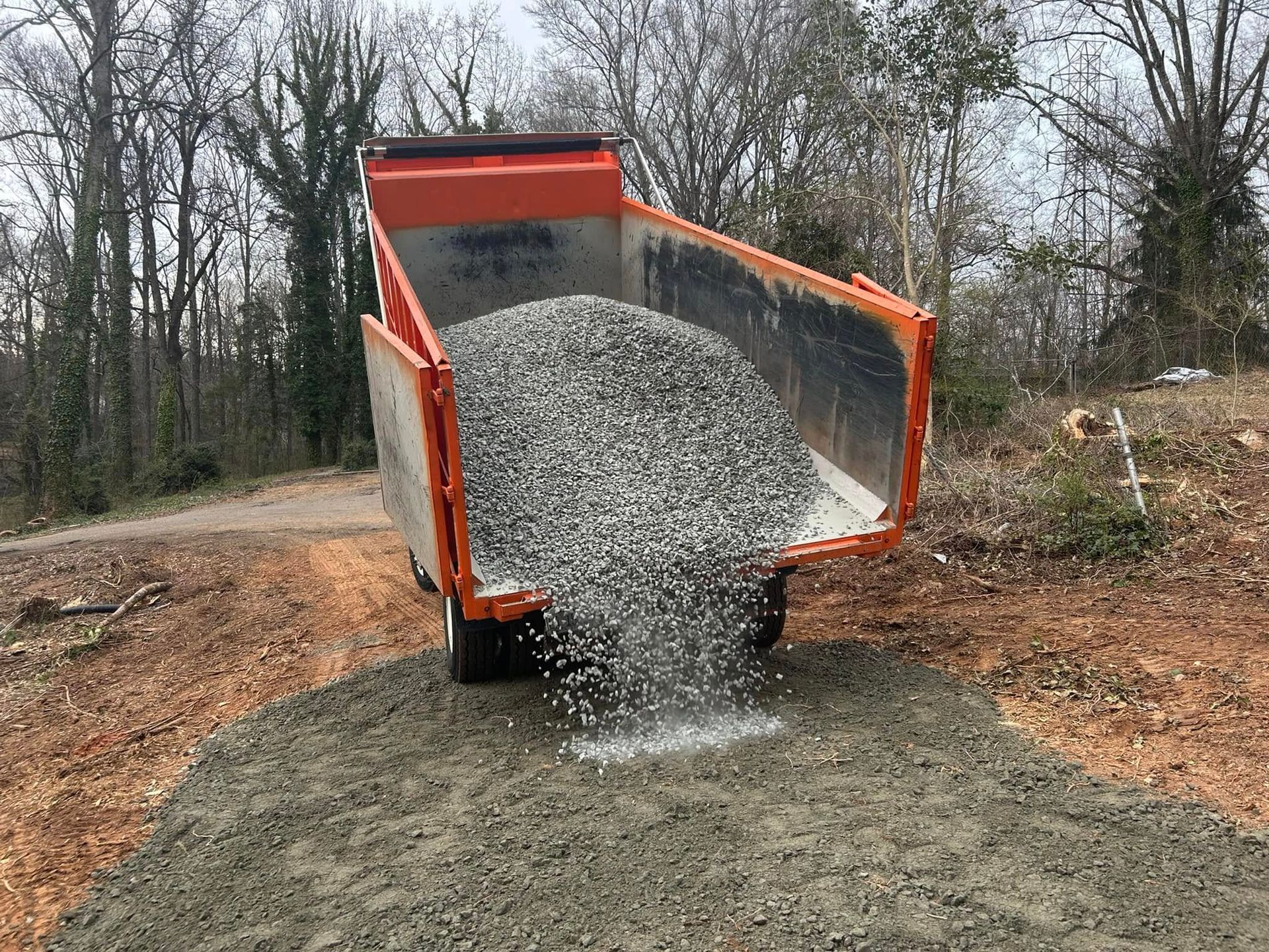 Orange dump truck unloading gravel onto a dirt road