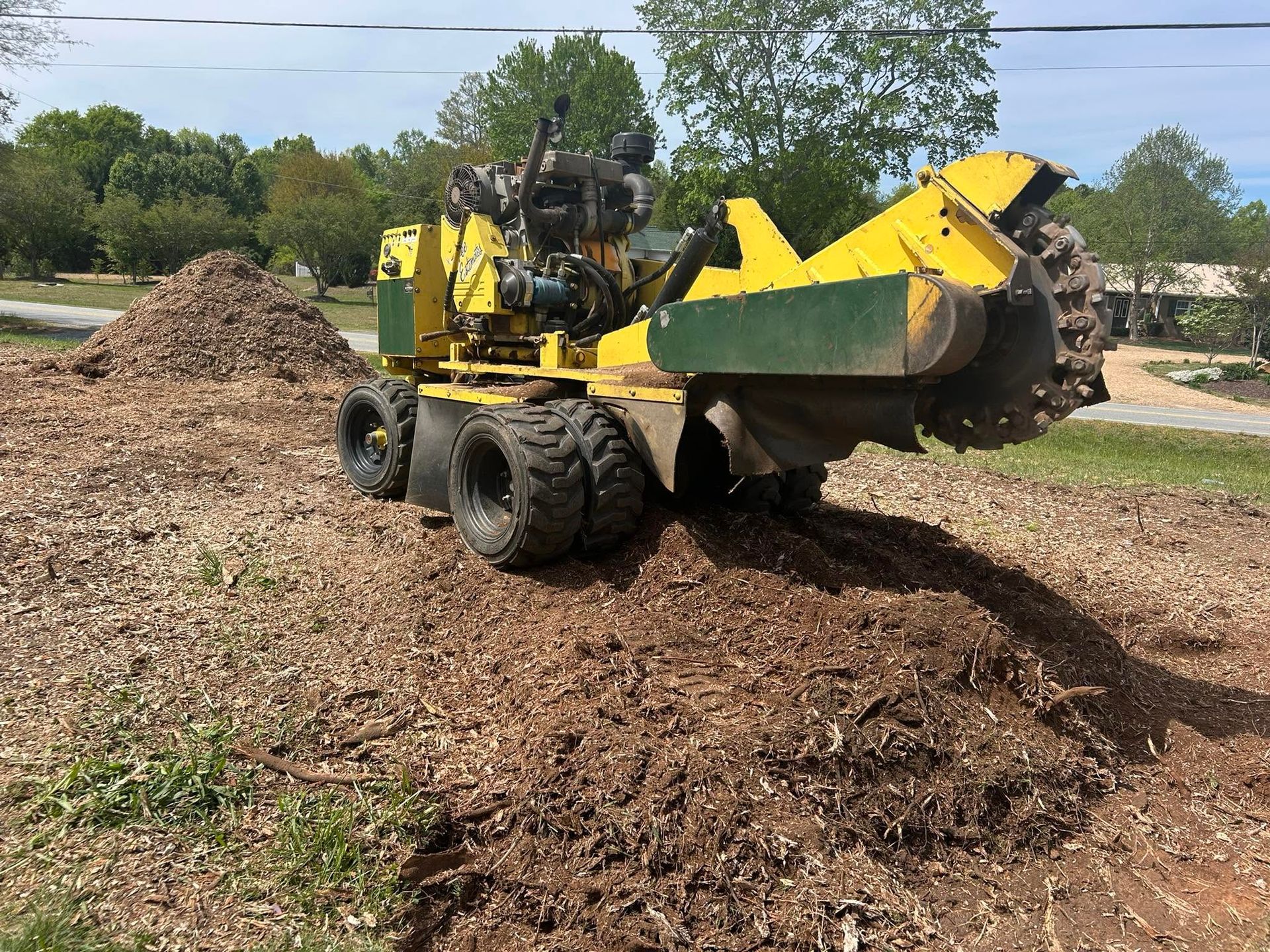 Yellow mulch-moving machine on a wood chip pile in an outdoor yard under a clear sky
