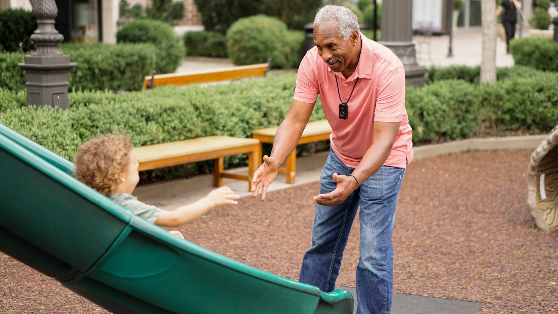 A man in a pink shirt is helping a child on a slide
