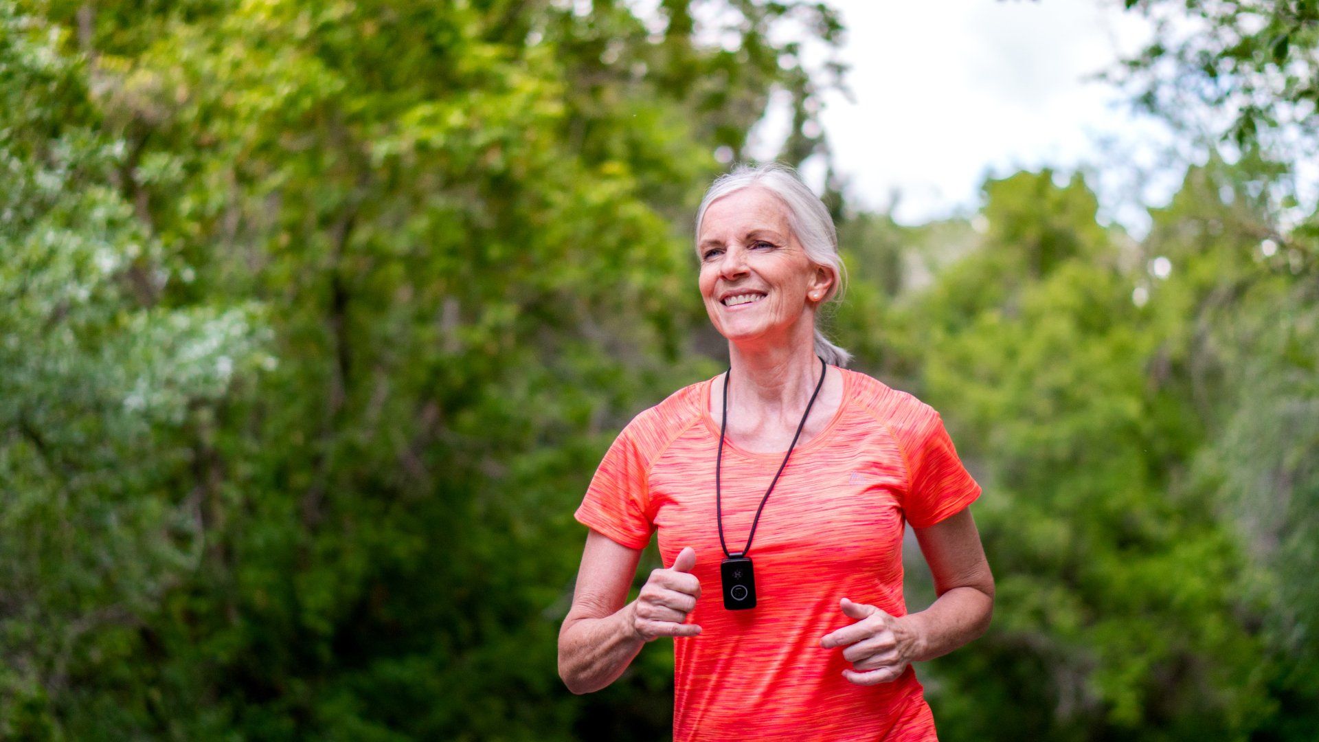 An elderly woman is running in a park with trees in the background.