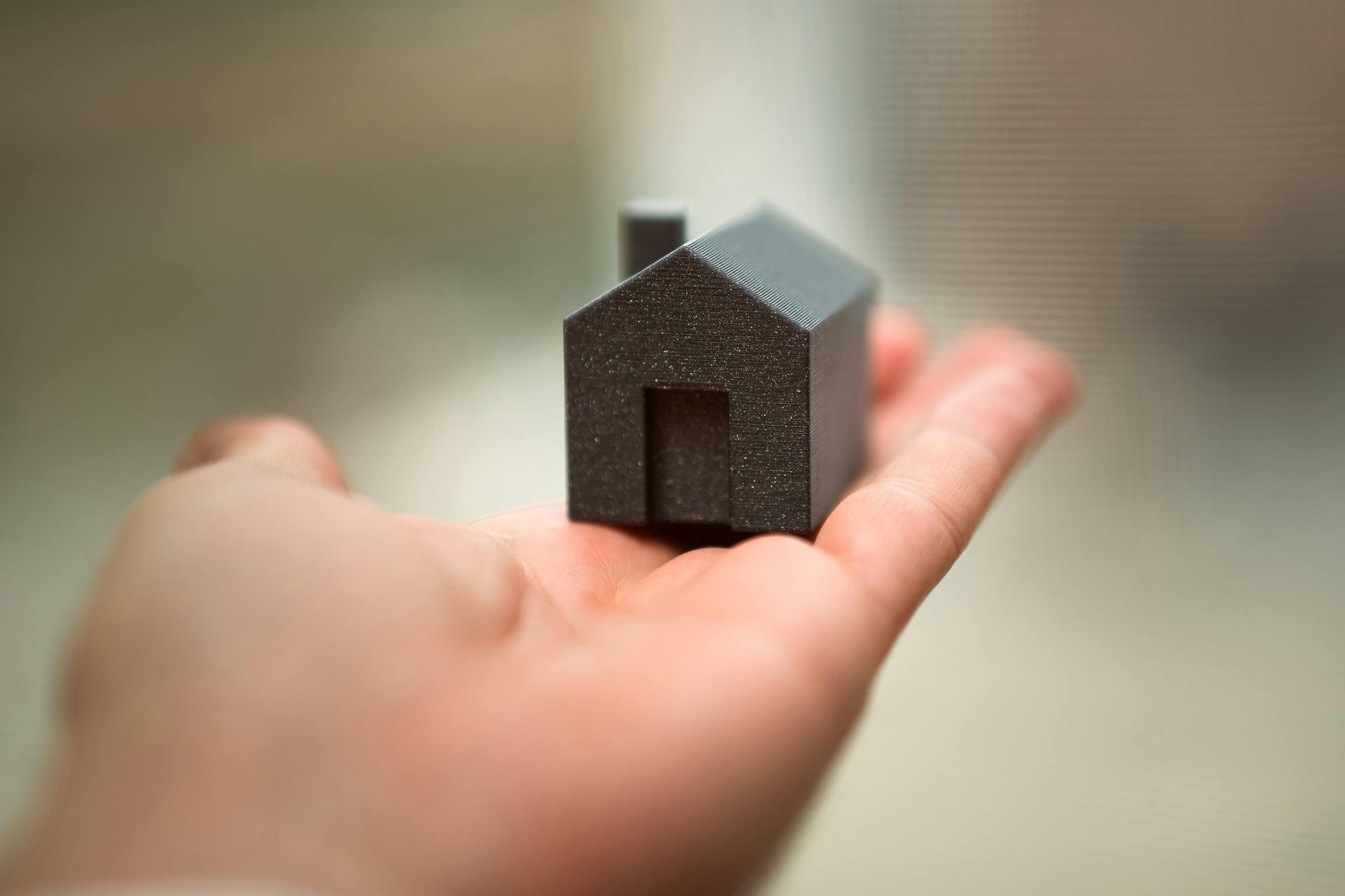 Hand holding a tiny dark house model against a blurred background