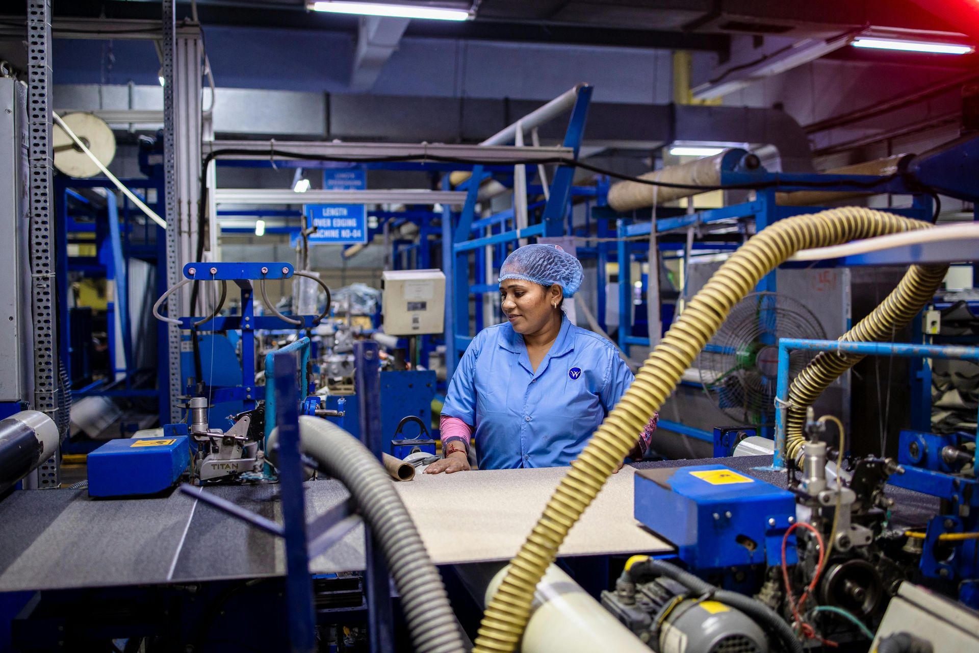 Worker in blue uniform operating machinery in an industrial factory with blue equipment and hoses