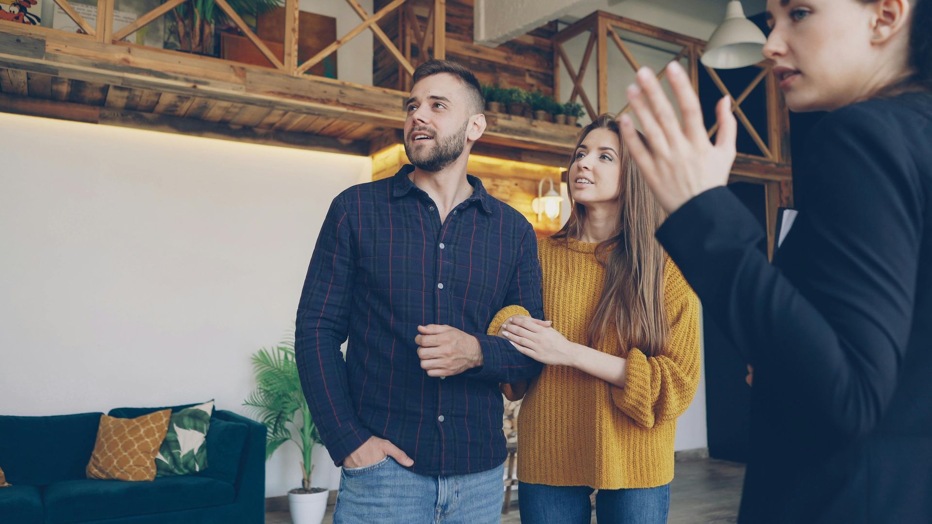 Three people standing in a loft office, one clapping while two smile and look ahead.