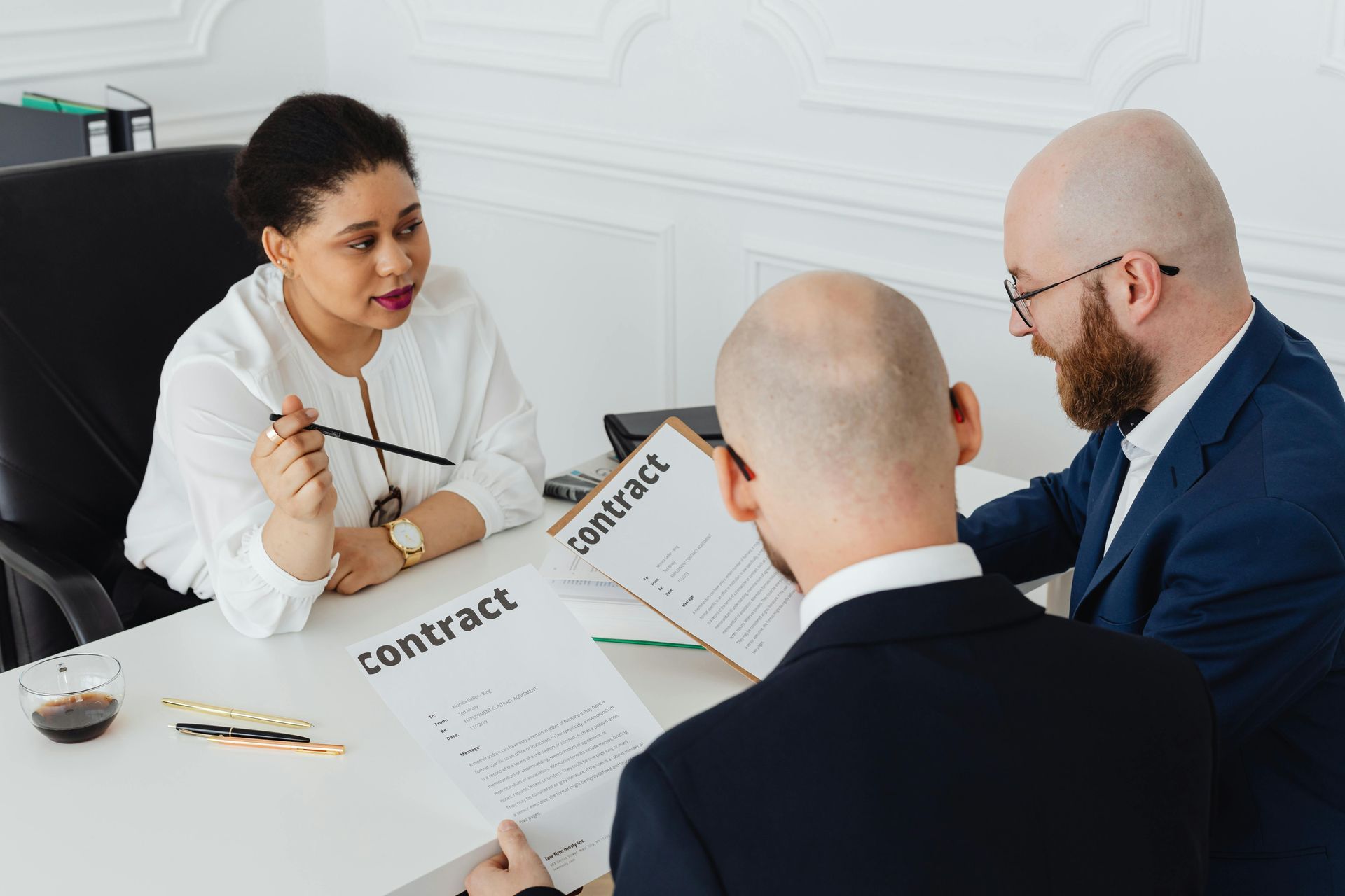 Three people review a contract during a business meeting at a white table.