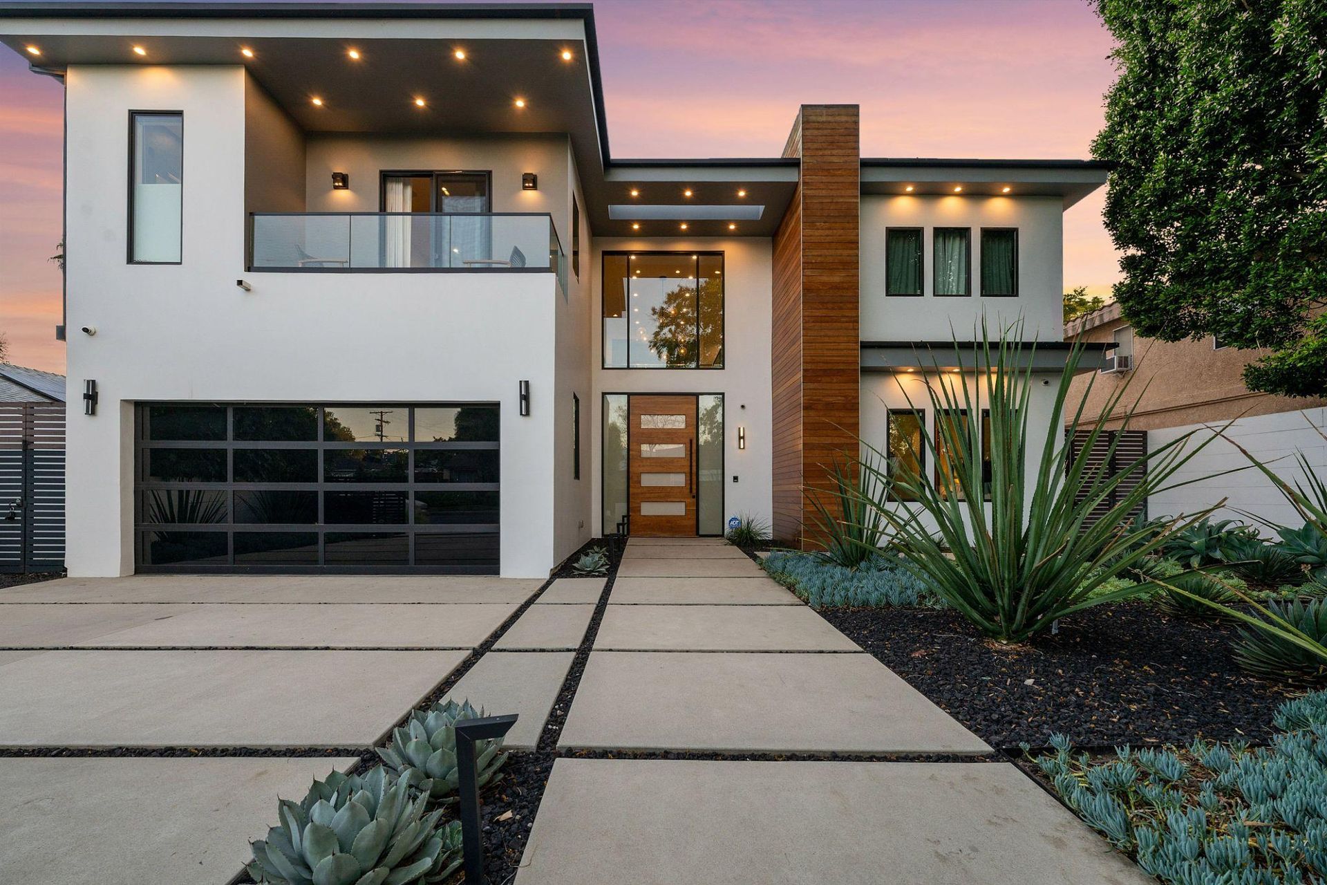 Modern two-story house with a glass garage, front walkway, and desert landscaping at dusk