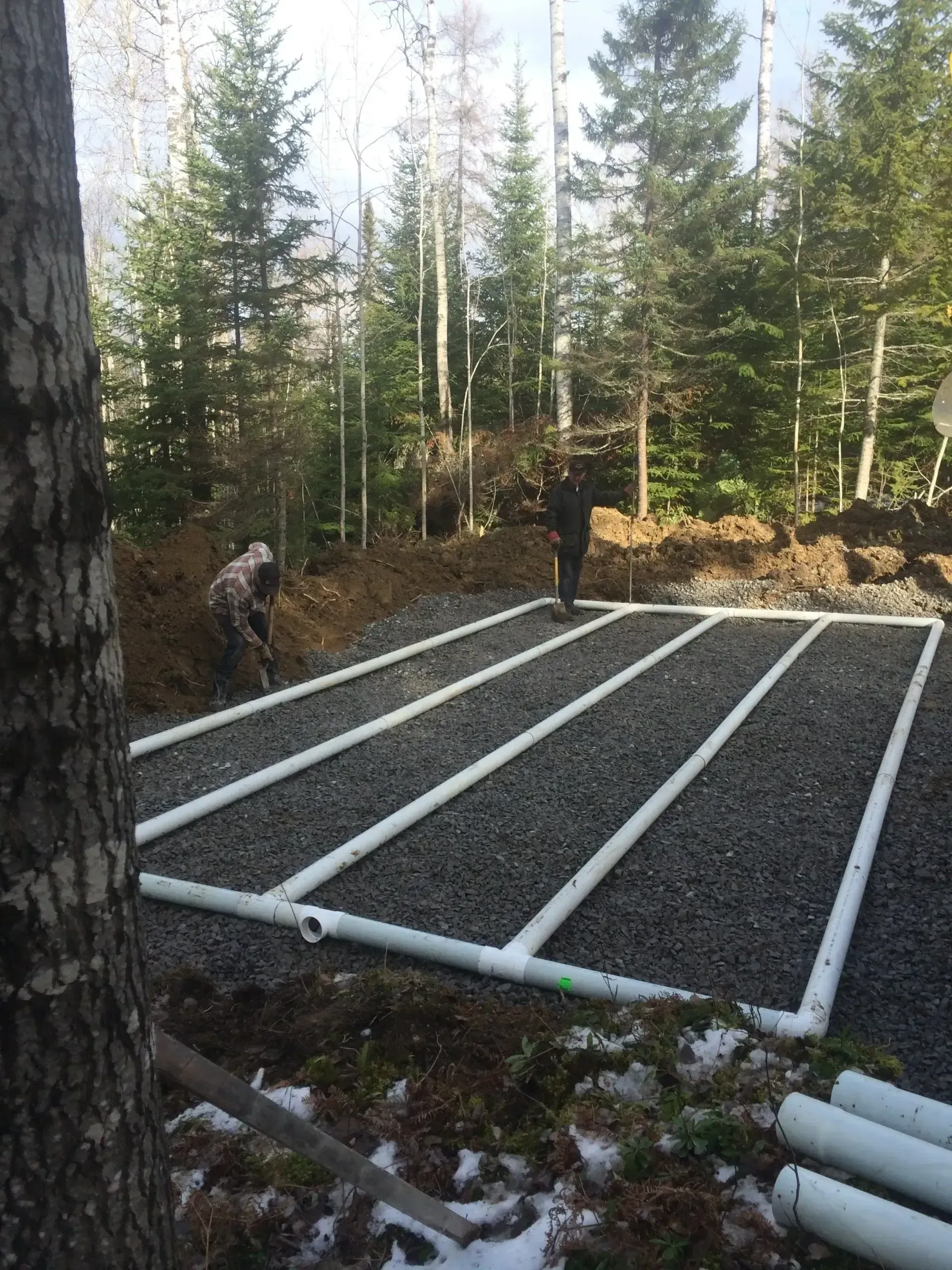 Travailleurs installant un champ d'épuration en tuyaux de PVC blanc sur un lit de gravier en forêt.