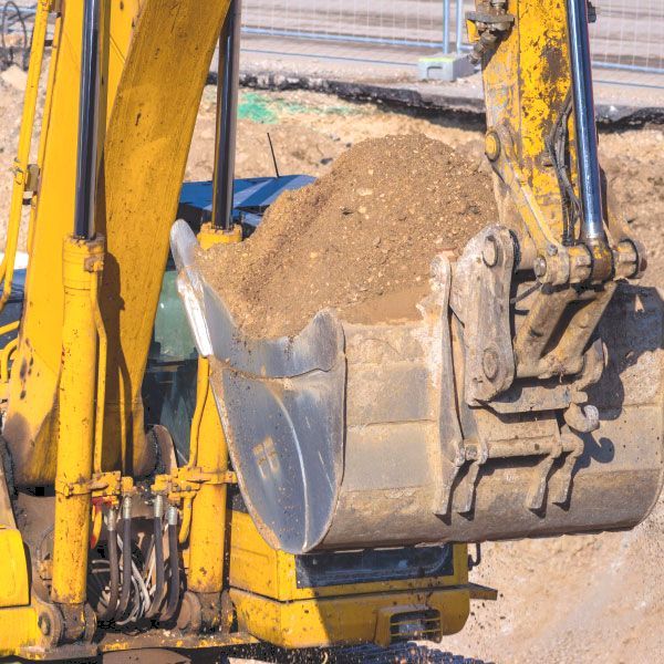 Gros plan sur le godet jaune d'une excavatrice déversant de la terre sur un chantier de construction