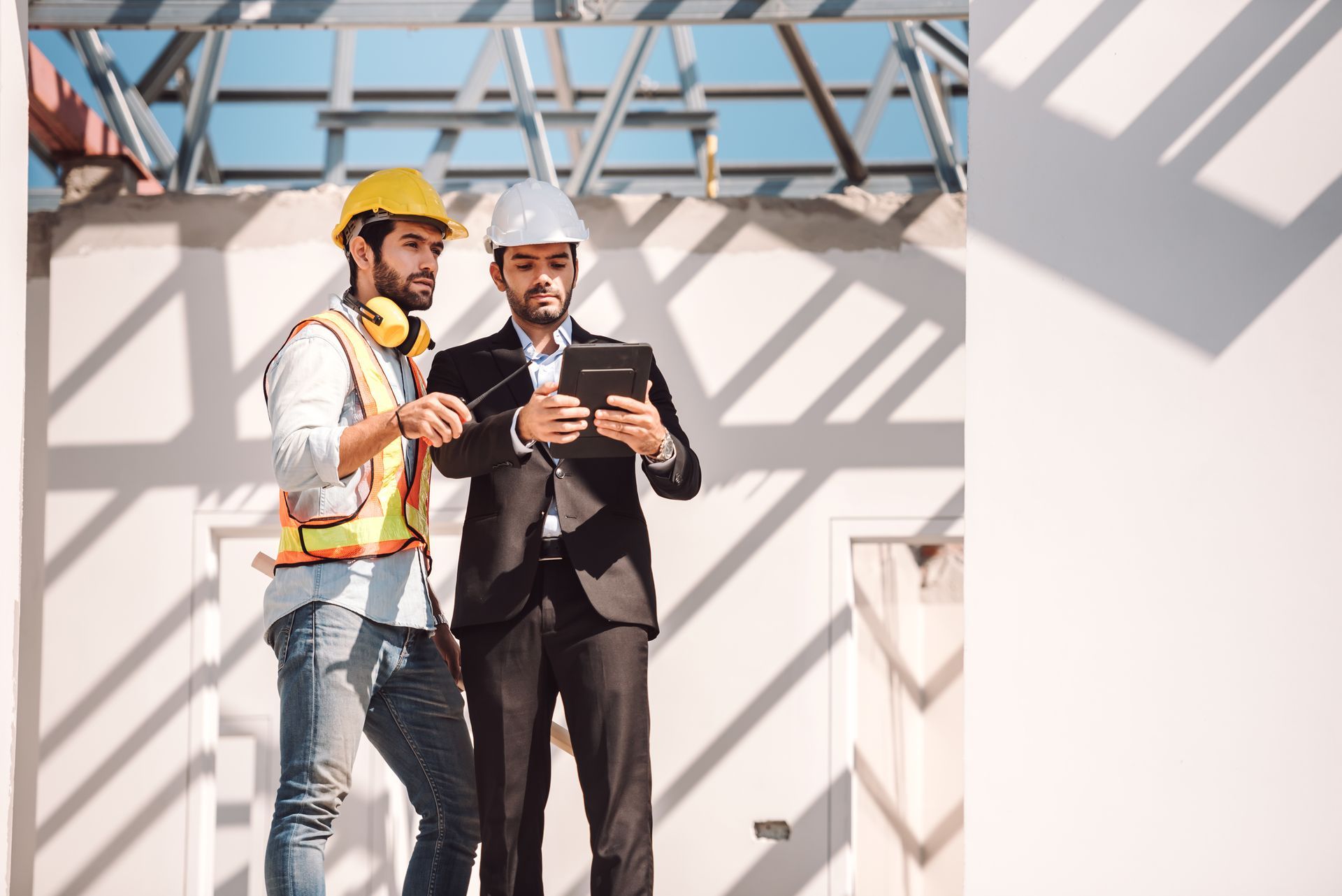 Two construction workers in hard hats reviewing a tablet on a building site