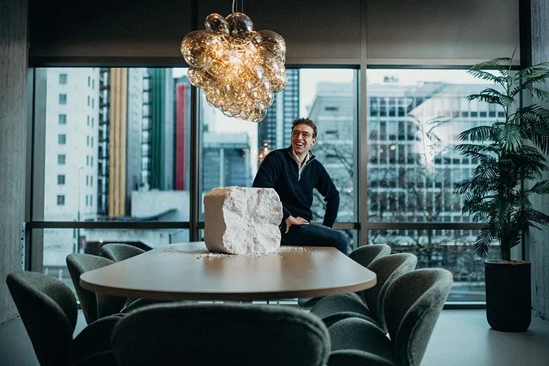 Mann sitter ved et bord med utsikt over byen, under en dekorativ lampe.