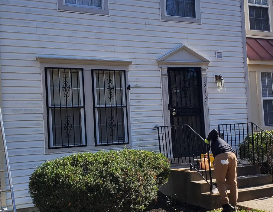 Person using a pressure washer on the steps of a white townhouse with black security bars.